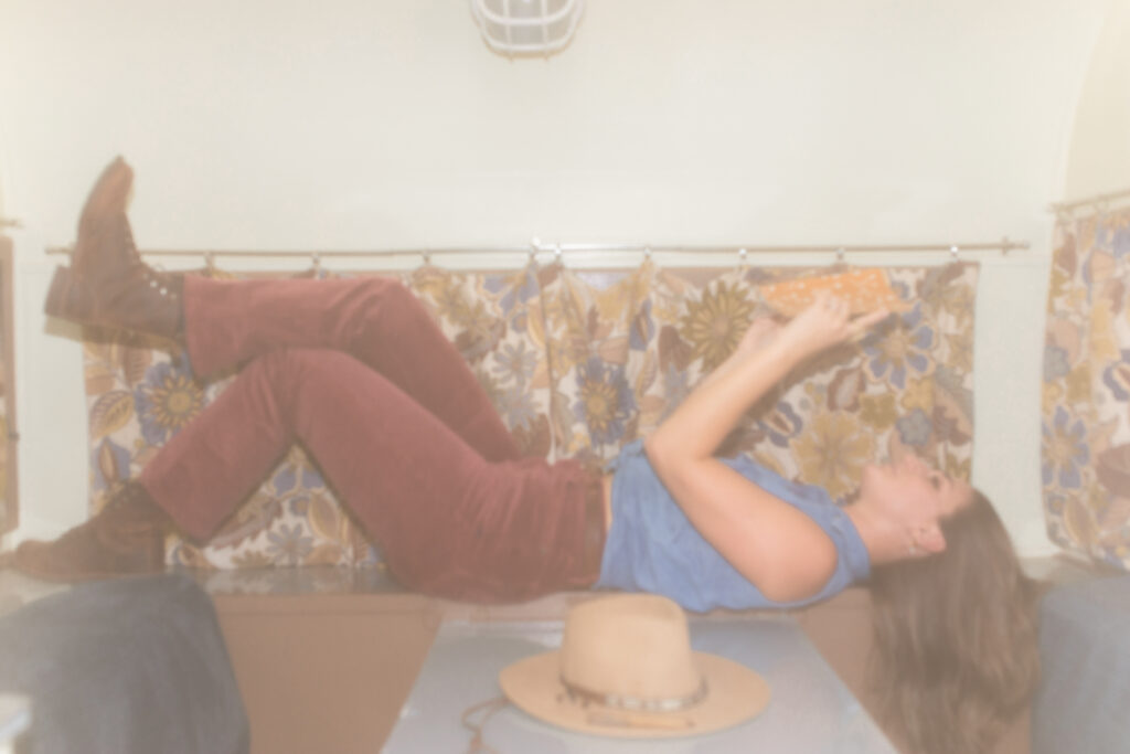 A small business copywriter lays across a 1970s RV table, reading a book about copywriting strategy.