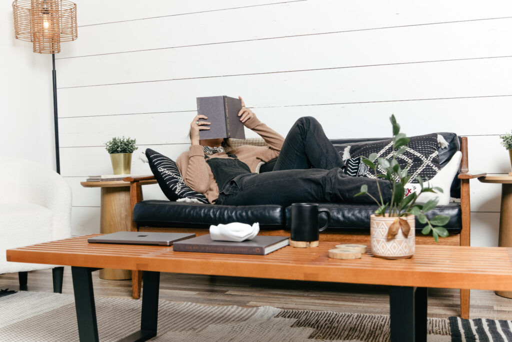 A copywriter lounges on the couch while reading a book about strategic copywriting.