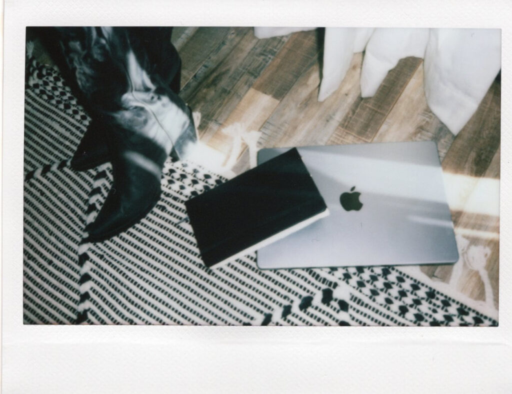 A laptop and journal are splayed on the floor next to a copywriter's black boots–both are used in small business blog strategy.