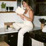 A small business copywriter reads a book while sitting on a kitchen counter.