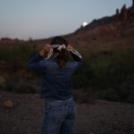 A sales copywriter for small businesses ties up her hair in a white and black bandana while looking at the desert.