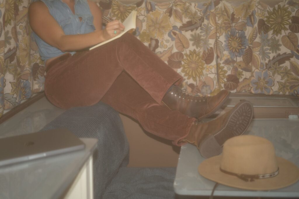 A pro copywriter writes a few notes in a journal while sitting in a 70s retro camper.