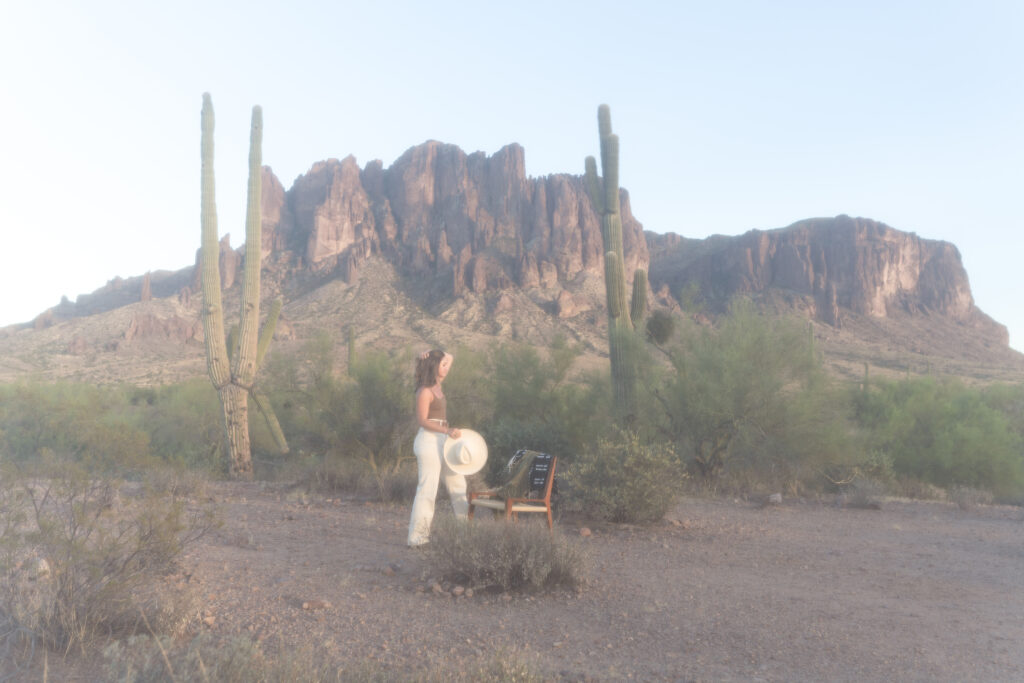 A blogger walks towards an empty chair in the Arizona desert, looking out over the vacant landscape near cacti and mountains.