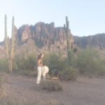 A blogger walks towards an empty chair in the Arizona desert, looking out over the vacant landscape near cacti and mountains.