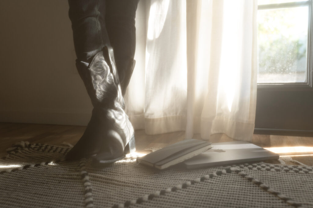 A copywriter in black boots stands next to a laptop, where she fine-tunes brand voice for clients.